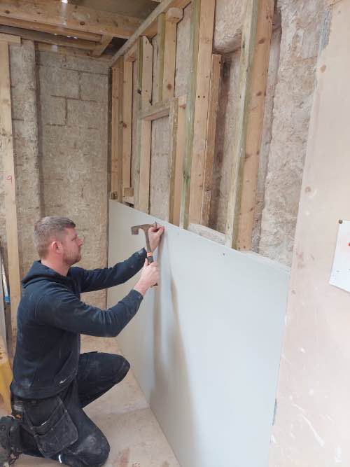 person fixing plasterboards to a stud wall
