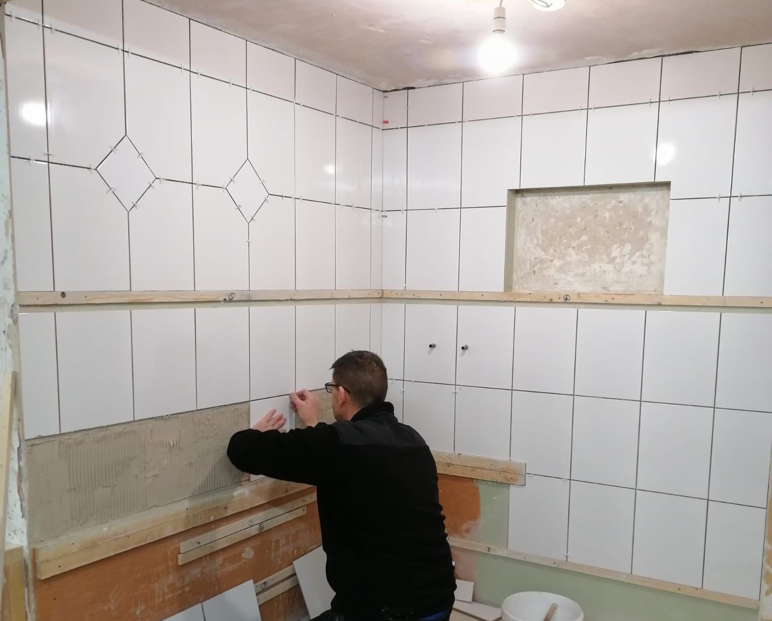 person fixing tiles to adhesive on a wall