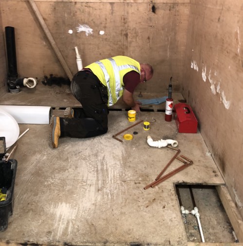 person installing copper pipe under flooring