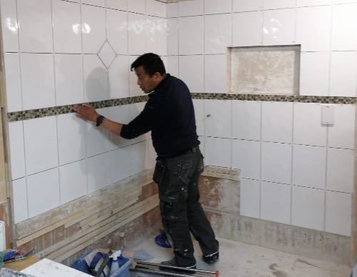 person fixing mosaic tiles to a wall area